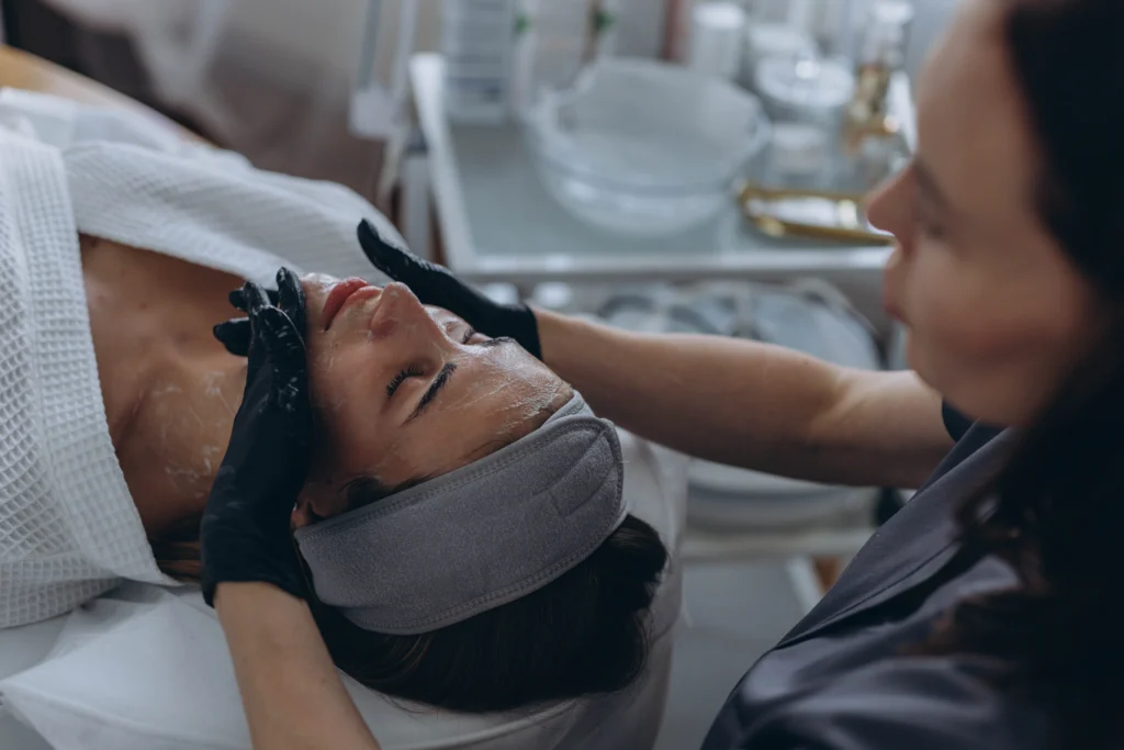 Una especialista de Lozania Centro Estético realiza una limpieza facial en un paciente, aplicando con cuidado productos para el cuidado de la piel. La escena refleja un enfoque en la medicina estética facial y tratamientos no quirúrgicos, subrayando la importancia de la evaluación médica personalizada y el uso de tecnología estética avanzada. El paciente se encuentra acostado cómod